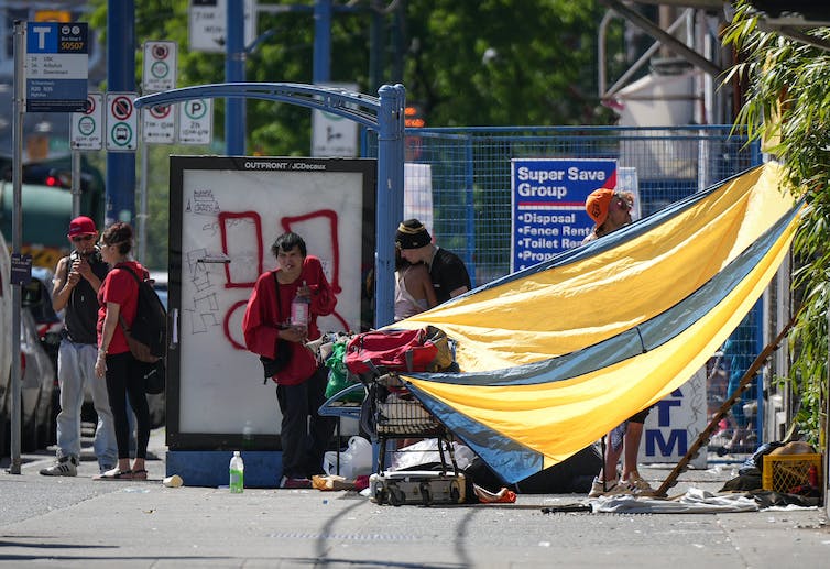 A tarp is tied up to provide shade against the sun while a group of people stand nearby.